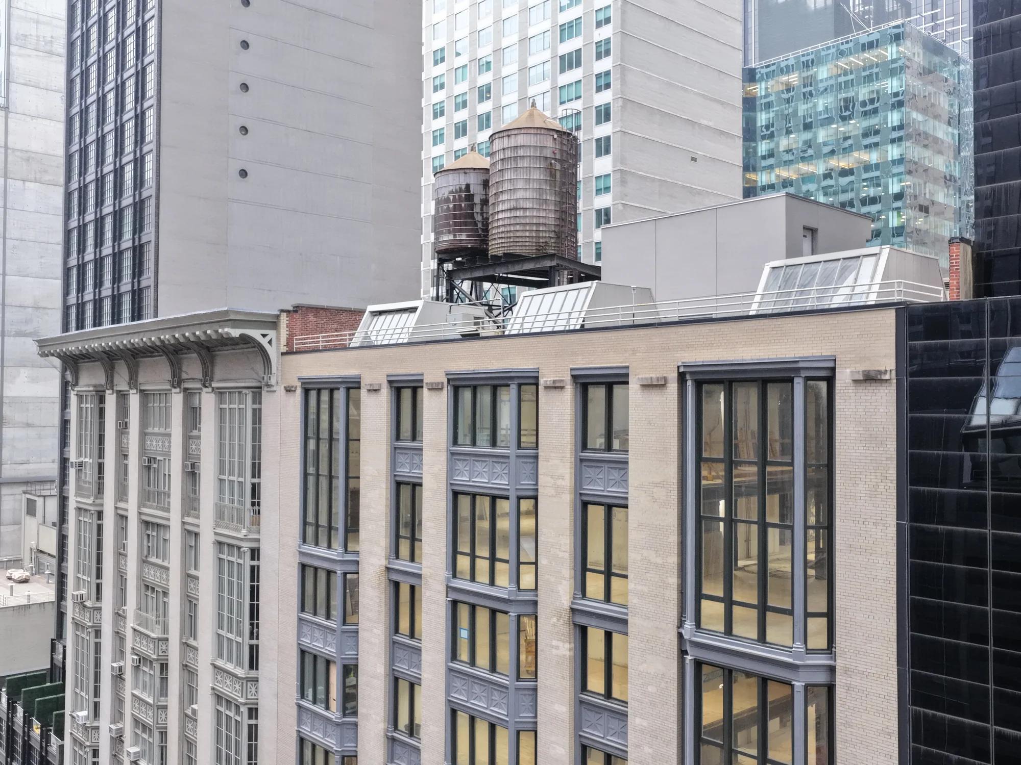Aerial view of the cornice and roofline from across the street, with two water tanks and taller Midtown buildings behind