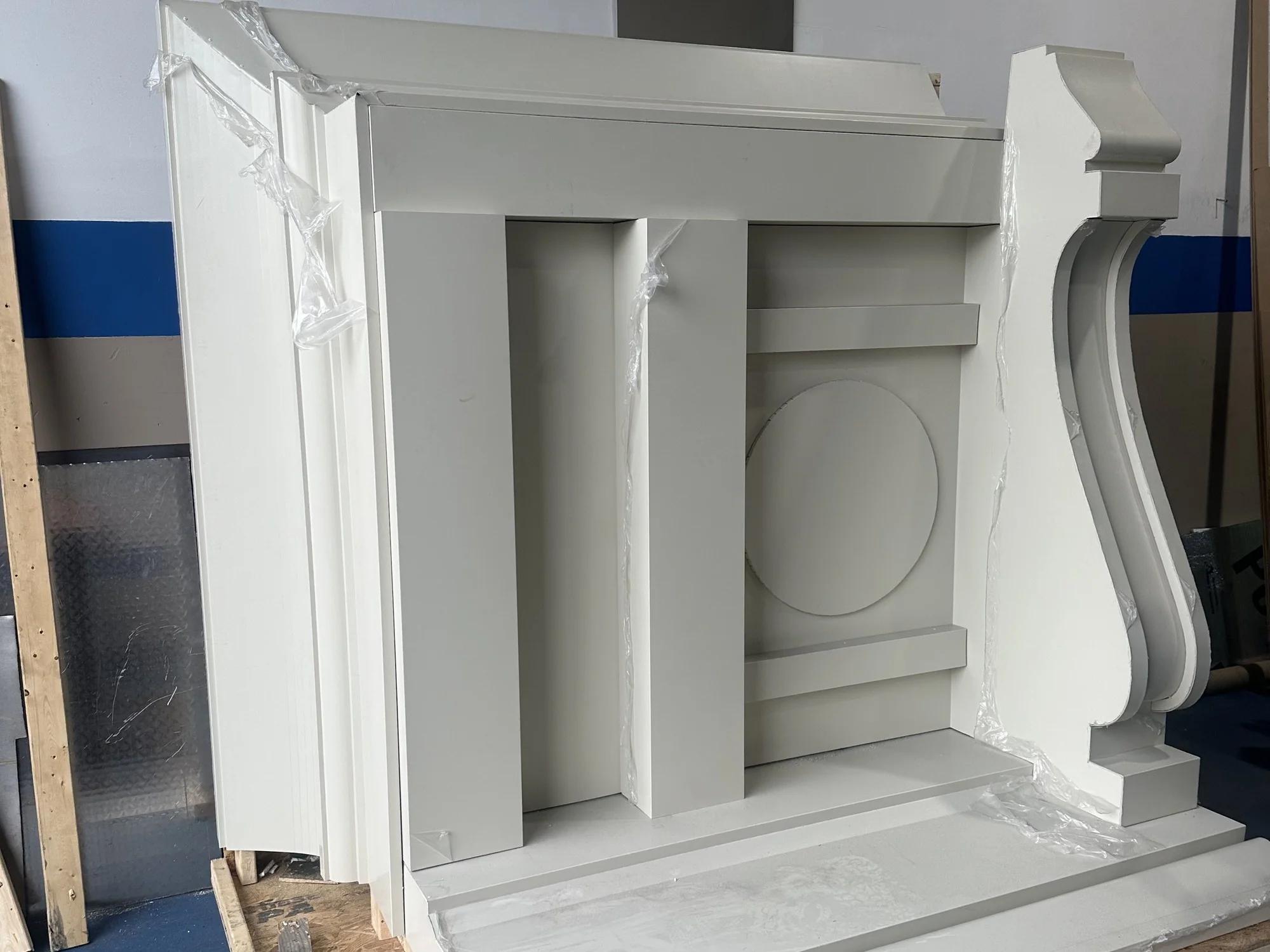 A replacement cornice bracket section in grey primer, standing on a shop floor before installation