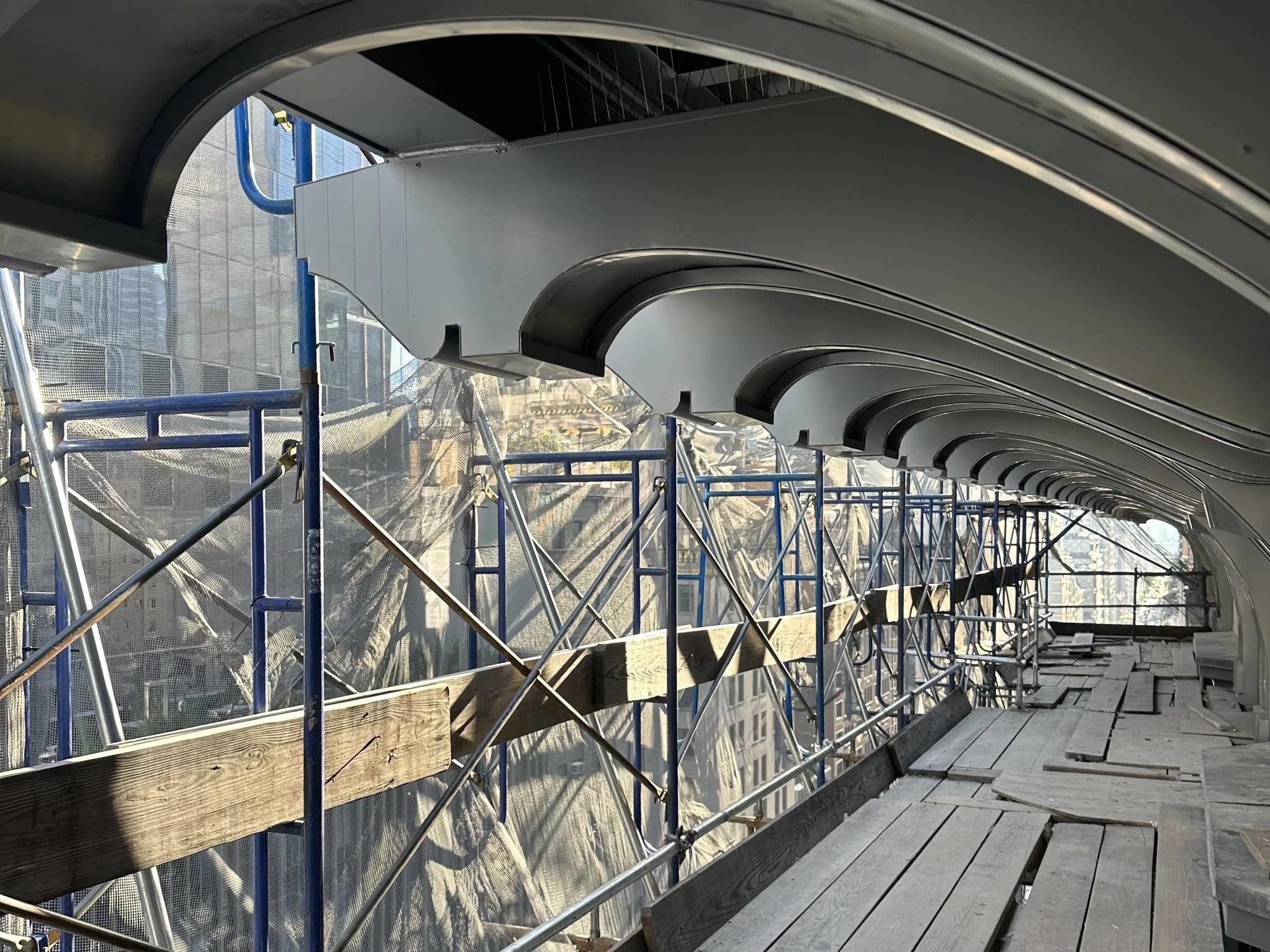 The cornice run seen along the scaffold, its curved brackets overhead and protective netting on the outside
