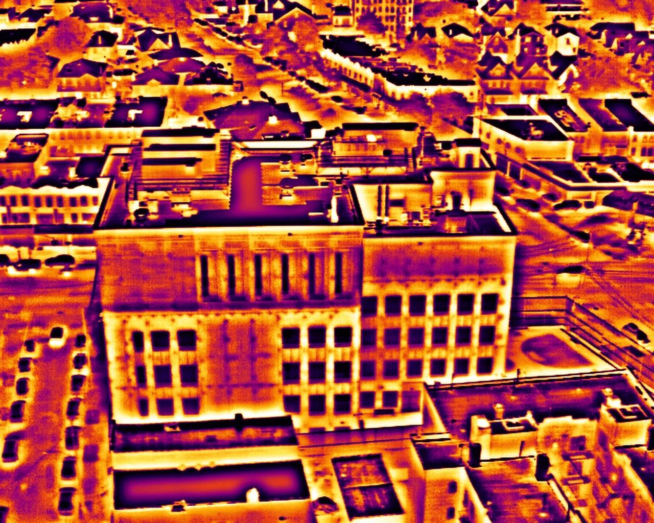 Aerial thermal frame of the low-rise building in the ironbow palette, warm areas in orange and yellow on a dark blue ground