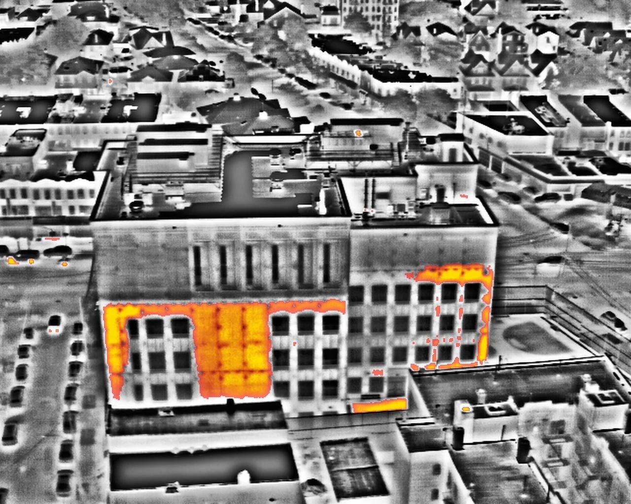 The same aerial thermal frame in the red-hot palette, the warmest areas in red over a greyscale image