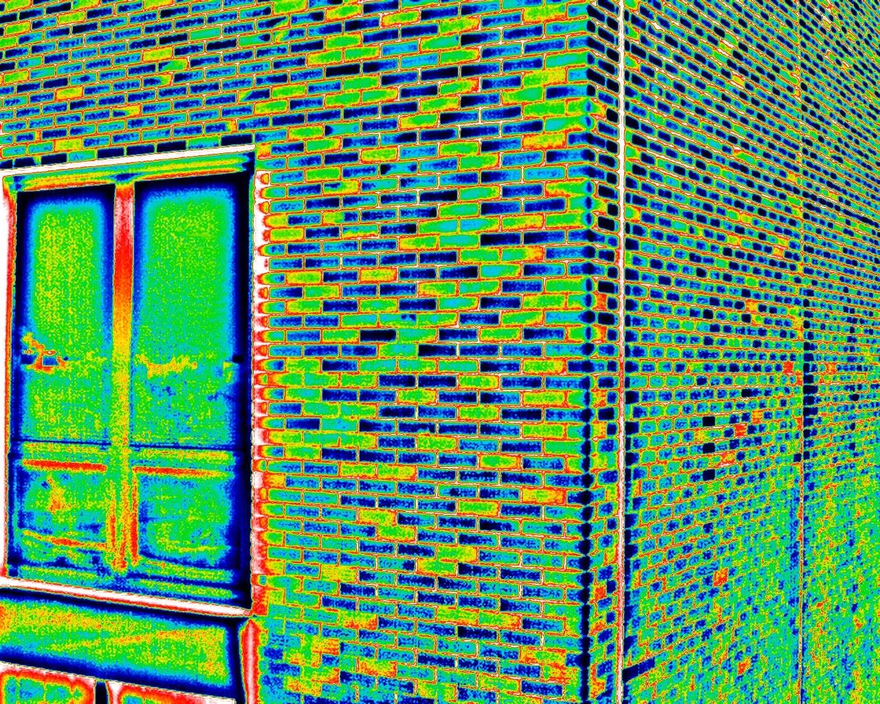 Close-range thermal frame of a brick wall beside a window in the rainbow palette, temperatures mapped across blue, green, yellow and red