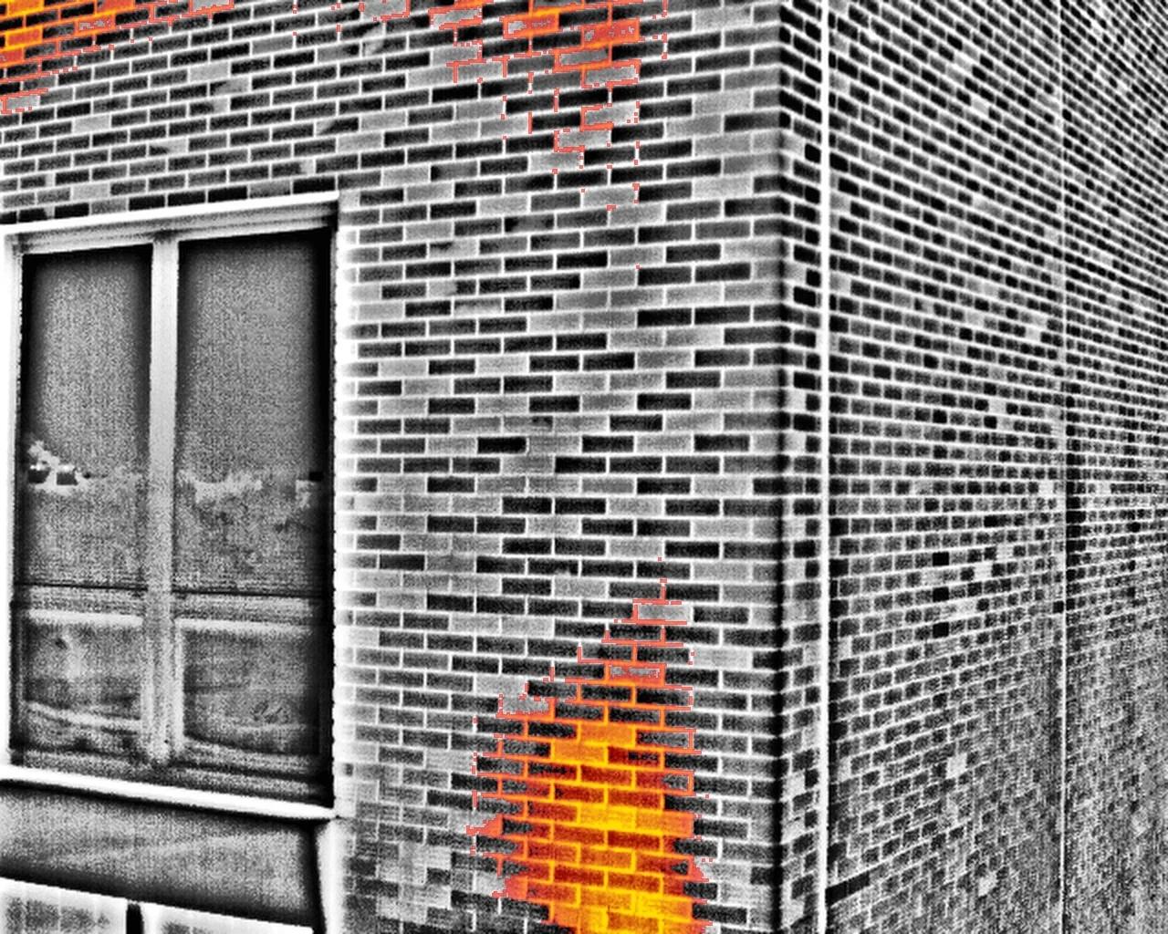 The same close-range frame in the red-hot palette, the warmest patch of brickwork in orange over a greyscale image