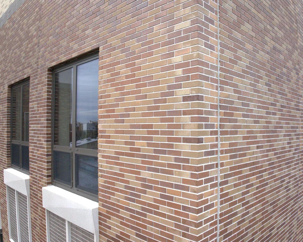 The same brick wall and window in visible light: tan and brown brickwork, a dark-framed window, and the corner of the building