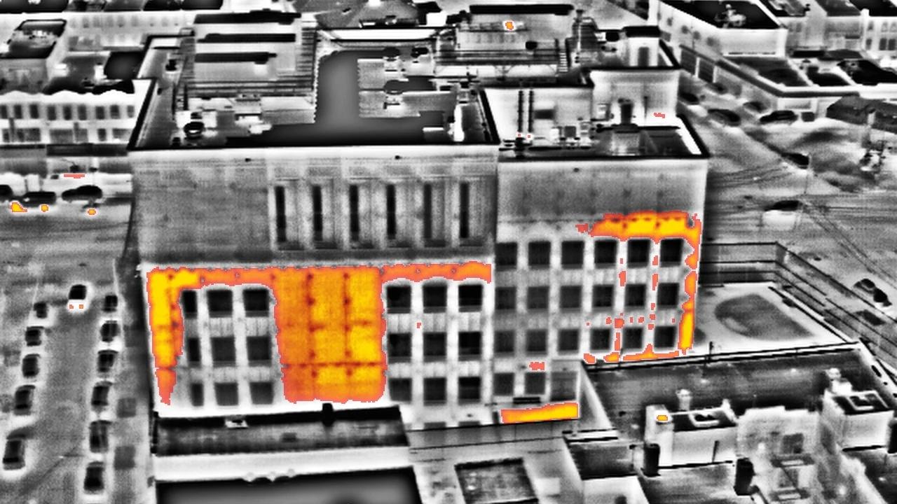 Aerial thermal image of a low-rise building, warm areas of the façade in orange and yellow against grey surroundings